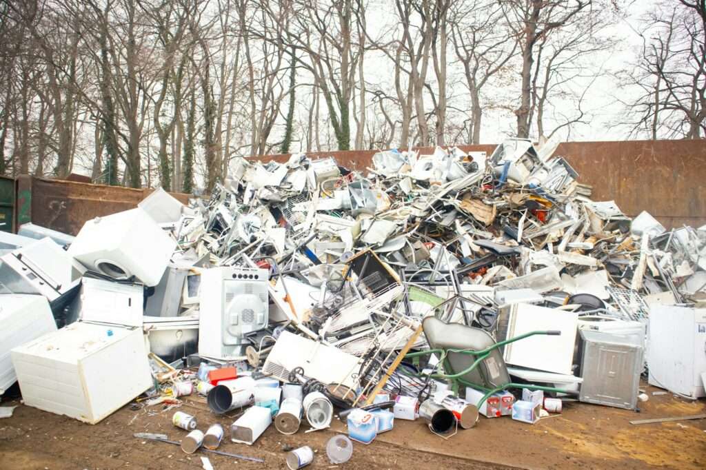 schrotthändler hannover Ein großer Haufen ausrangierter Haushaltsgeräte, darunter Waschmaschinen, Trockner und Mikrowellenherde, ist auf einem Schrottplatz aufgehäuft. Mit kahlen Bäumen im Hintergrund, die eine winterliche Landschaft andeuten, könnte man sich fragen, wie hoch die aktuellen Schrottpreise in Hannover für all diesen Schrott sind. metallschrott hannover