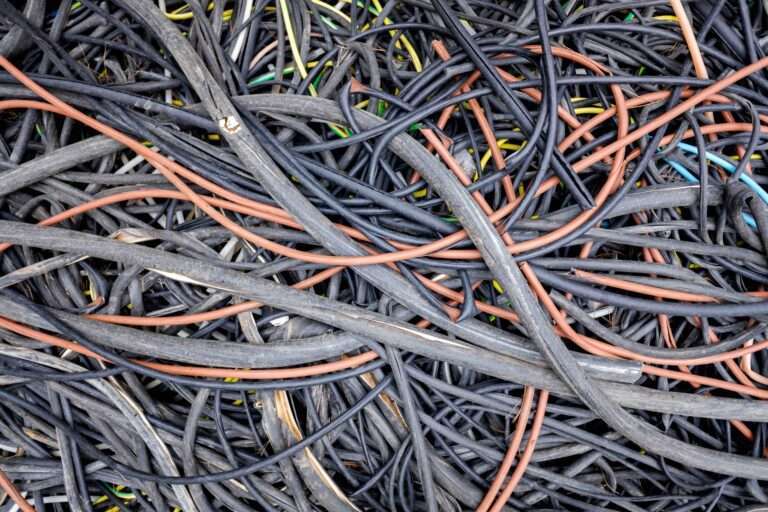 schrotthändler hannover Ein Wirrwarr aus zahlreichen schwarzen, roten und gelben Kabeln und Drähten, das an „Schrott zum Abholen“ erinnert. Die Kabel sind ineinander verschlungen und bilden ein chaotisches Muster. Einige Abschnitte der Kabel sind teilweise von anderen Kabeln mit unterschiedlicher Dicke und Länge bedeckt. metallschrott hannover